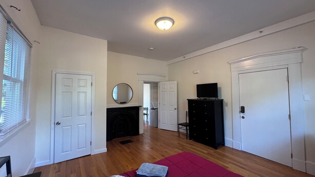 A spacious living room with hardwood floors, a fireplace, a television on a stand, and a door leading to another room. - Updated 1BR apt, 1st floor, near T, free parking (Malden)