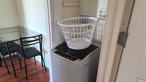 A laundry room with a washing machine and a basket on top. There is a table with chairs in the adjacent room. - Updated 1BR apt, 1st floor, near T, free parking (Malden)