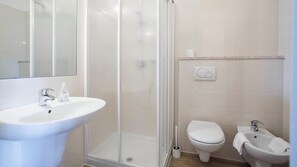 Ein Badezimmer mit Waschbecken, Toilette, Bidet und einer Duschkabine aus Glas.