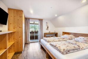 Ein Schlafzimmer mit Holzschrank, einem Bett mit floralem Bettzeug, einem Fernseher an der Wand und einem Fenster mit Vorhängen.