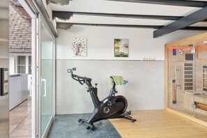 Ein modernes Fitnessstudio mit Fahrradergometer, Sauna und einer Glastür, die auf eine Terrasse führt.