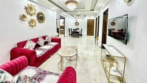 Ein modernes Wohnzimmer mit einem roten Sofa, einer Chandelüster, einem Deckenventilator und einem an der Wand befestigten Fernseher.