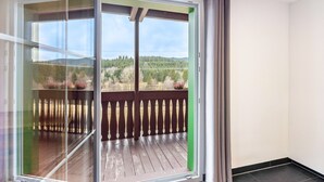 Een balkon met een houten terras, een glazen deur en uitzicht op een bebost landschap.