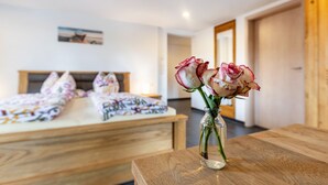 Een slaapkamer met een bed, een houten nachtkastje en een vaas met bloemen.