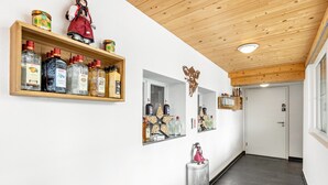 Een gang met houten plafond, een witte deur en planken met flessen en een pop.