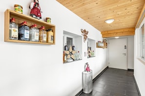 A hallway with wooden ceiling, a white door, and shelves with bottles and a doll. - Speckhuisli – Mettmablick Comfort with Balcony, Breakfast, Sauna, Mountain View, Inn (Grafenhausen)