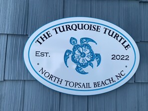 Un panneau circulaire sur lequel on peut lire les inscriptions « The Turquoise Turtle » et « North Topsail Beach, NC », le tout sur un fond en bois.
