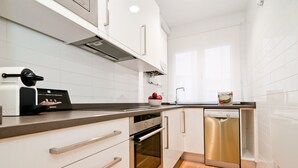 Een moderne keuken met witte kastjes, een ingebouwde oven, een vaatwasser en een koffieapparaat.