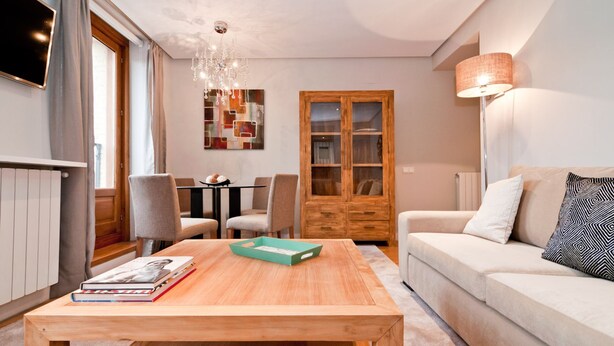 Een woonkamer met een houten salontafel, een bank, een eettafel met stoelen, een kast en een tv die aan de muur hangt.