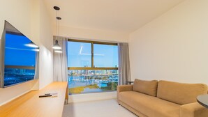 A modern living room with a large window, a sofa, a TV, and a wooden table. - Parque do Cais #1210 - Apt With a View by Carpediem (Recife)