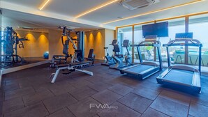 A modern gym with cardio machines, weightlifting equipment, and a large window offering a view of the outdoors. - Parque do Cais #1210 - Apt With a View by Carpediem (Recife)