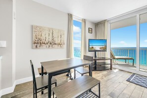 Et moderne værelse med et spisebord, stole, et fjernsyn og en balkon med havudsigt.