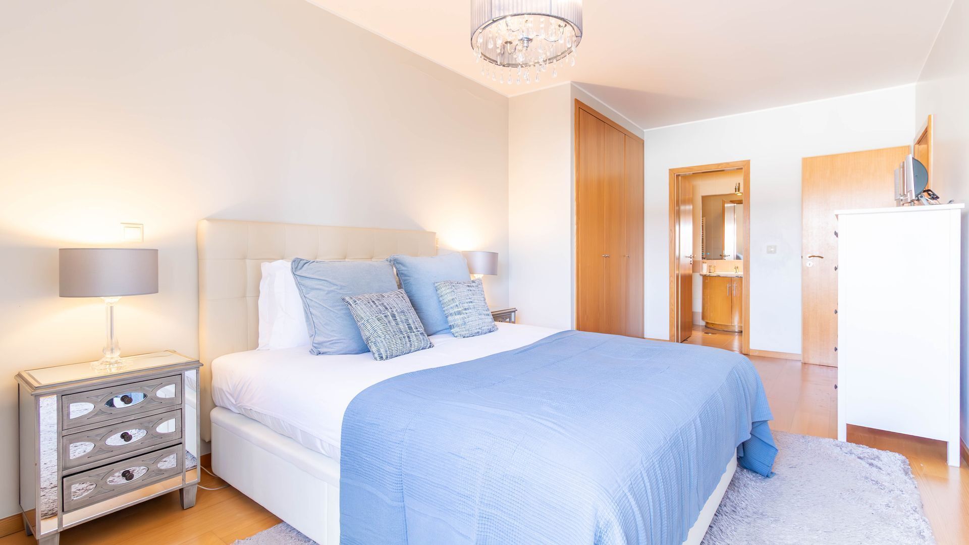 Quarto com cama, mesas de cabeceira, cômoda, lustre e guarda-roupa.