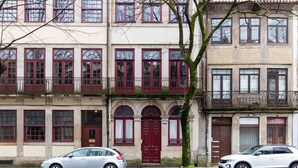 A row of multi-story buildings with red-framed windows and balconies, parked cars in front, and a tree in the foreground. - B. Arts IV by LovelyStay (Porto)