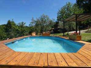 Une piscine rectangulaire avec une terrasse en bois, entourée d’arbres et dotée d’un espace abrité.
