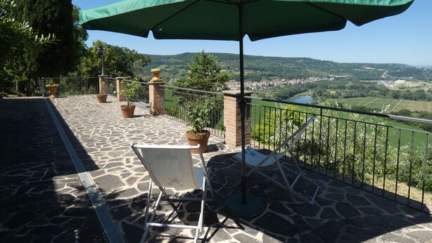 A terrace with a stone floor, a green umbrella, potted plants, and a view of a valley. - Scappo in Umbria, Antico casale (Umbria)