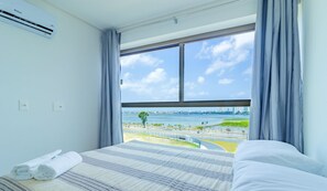 A hotel room with a large window, a bed with striped bedding, and a view of a waterfront and cityscape. - Parque do Cais #308 - Recife By Carpediem (Recife)