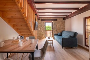 A cozy room with a wooden staircase, a stone wall, a sofa, and a dining table with chairs.