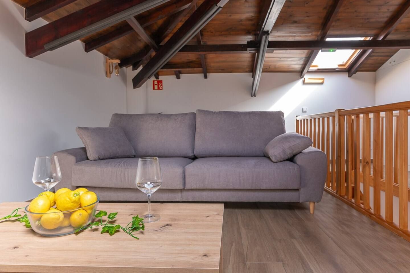 Un salon avec un canapé gris, une table en bois sur laquelle se trouve un saladier en verre rempli de citrons, et deux verres à vin.