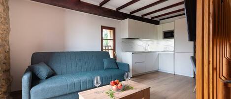 Una sala de estar moderna con un sofá, una mesa de centro de madera con fruta, y una cocina al fondo.