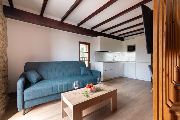 A modern living room with a sofa, a wooden coffee table with fruit, and a kitchen in the background.