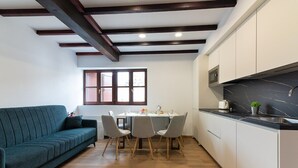 Una cocina moderna con encimera de mármol negro, vigas de madera en el techo, una zona de comedor con mesa y sillas, y un sofá verde.