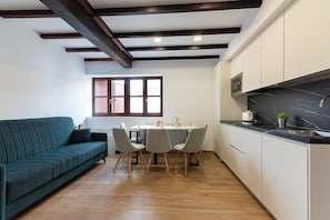 Eine moderne Küche mit schwarzem Marmor-Arbeitsplatz, Holzbalken an der Decke, einem Essbereich mit Tisch und Stühlen und einem grünen Sofa.