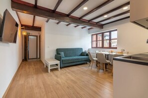 Un intérieur moderne avec un plancher en bois, un canapé de couleur turquoise, une petite table blanche et un coin cuisine avec une fenêtre.