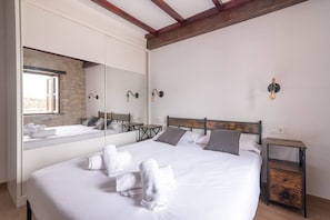 A bedroom with a large bed, a wooden headboard, a nightstand, a mirror, and a stone wall.