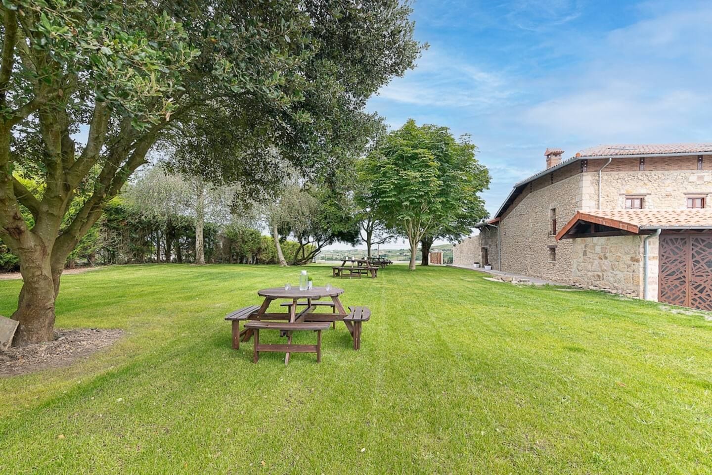 A grassy outdoor area with picnic tables and a stone building.