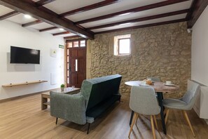 A room with a stone wall, a wooden ceiling, a television, a sofa, a table, and chairs.