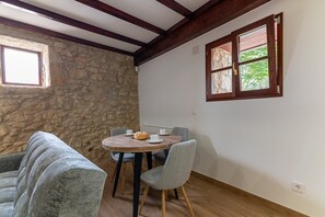 Una habitación con pared de piedra, techo de madera, una mesa redonda con sillas y una ventana con vistas a la vegetación.