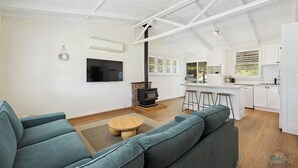 Una sala de estar moderna con un sofá grande, televisor, chimenea y una cocina con armarios blancos y un taburete de bar.