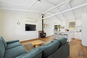 Ein modernes Wohnzimmer mit einer großen Couch, einem Fernseher, einem Kamin und einer Küchenzeile mit weißen Schränken und einem Barhocker.