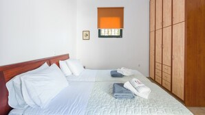 Ein Schlafzimmer mit zwei Betten, einem Kleiderschrank, einem Fenster mit Jalousien und einem kleinen Bild an der Wand.