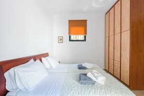 Ein Schlafzimmer mit zwei Betten, einem Kleiderschrank, einem Fenster mit Jalousien und einem kleinen Bild an der Wand.