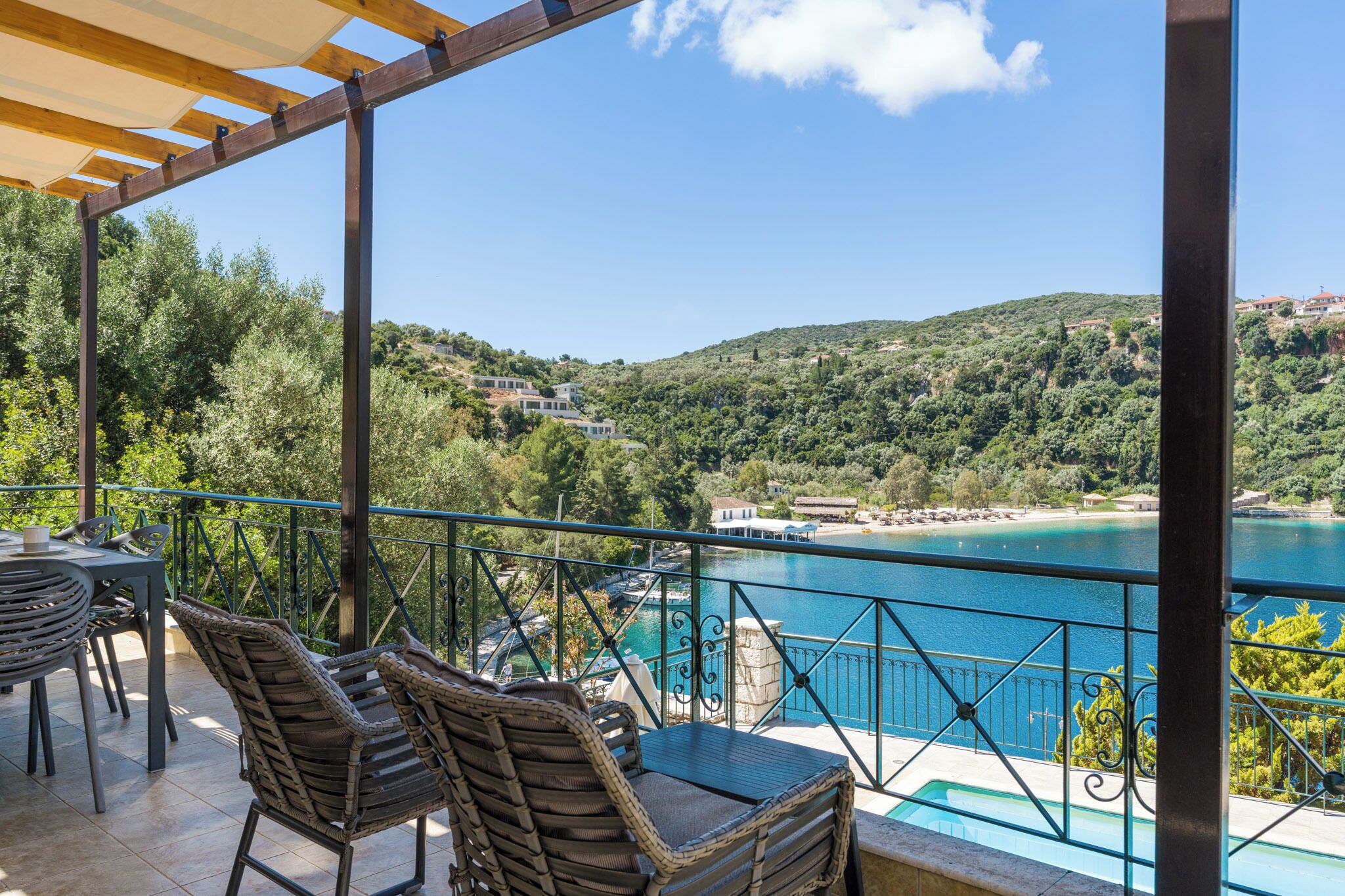 A terrace with wicker furniture, a pool, and a view of a lake and hills.