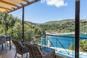 Eine Terrasse mit Korbmöbeln, einem Pool und Blick auf einen See und Hügel.