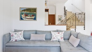 Ein Wohnzimmer mit grauem Sofa, floralen Kissen, einem Gemälde eines Bootes, einer Treppe und einer Holztür.