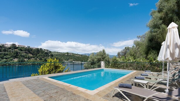 Ein Pool mit Liegestühlen und Blick auf einen See und Hügel.