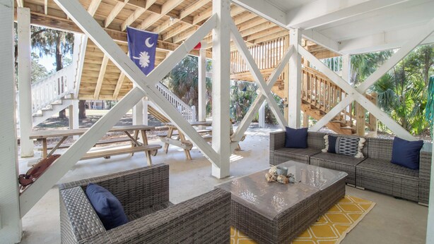 Un área de patio cubierta al aire libre con mobiliario de mimbre, una bandera y vistas del paisaje circundante.
