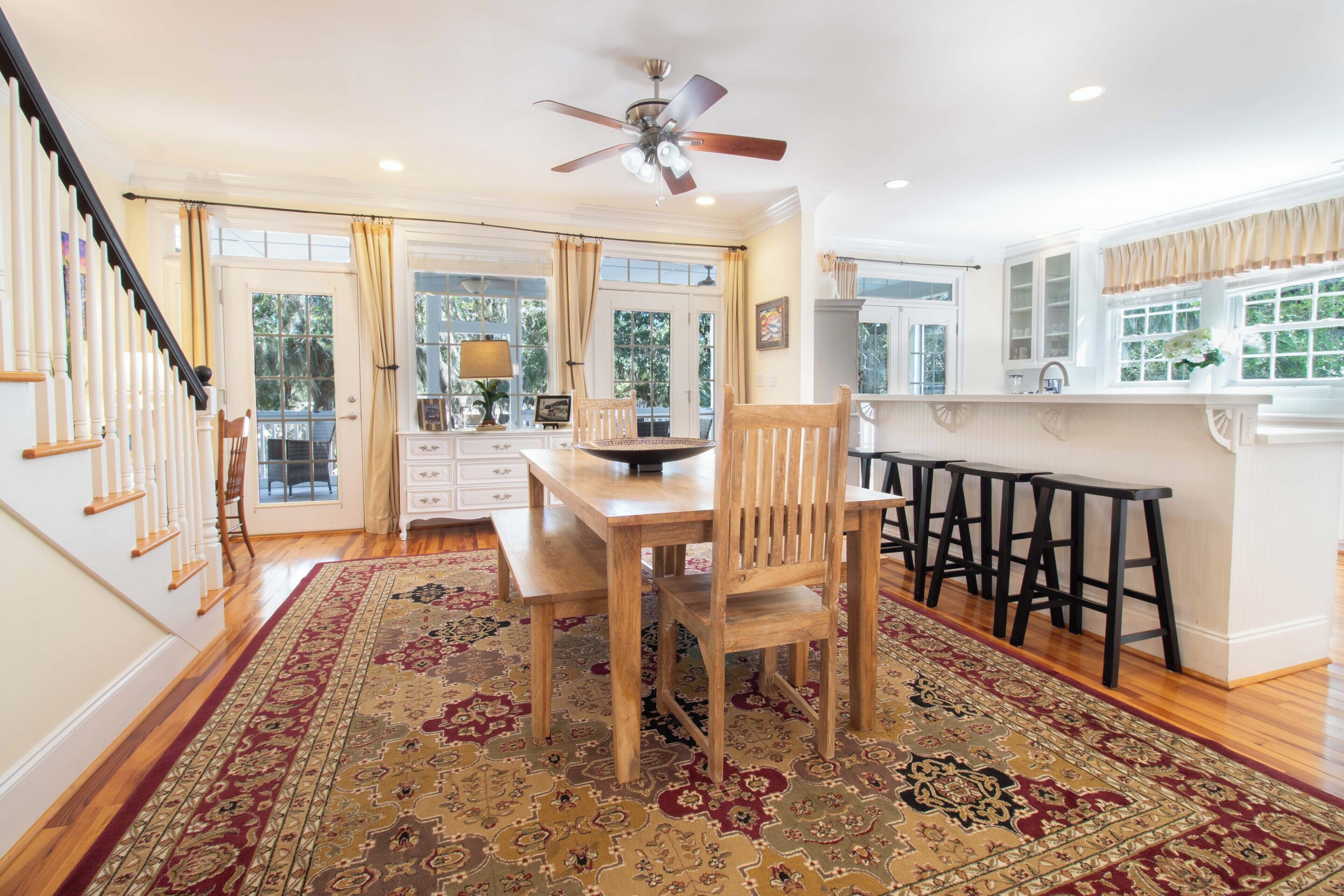 A spacious kitchen with a dining area, wooden chairs, a large rug, and a ceiling fan.