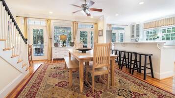 A spacious kitchen with a dining area, wooden chairs, a large rug, and a ceiling fan.