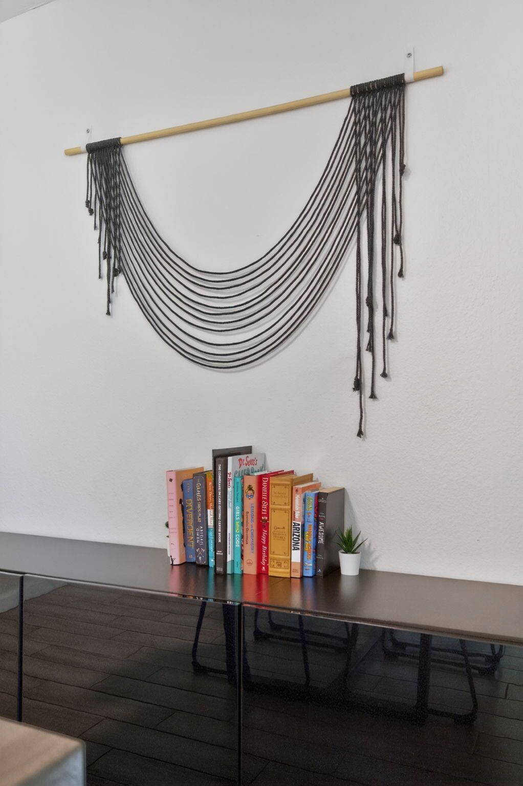 A room with a white wall, a wooden table with a black metal frame, and a black rope hammock.