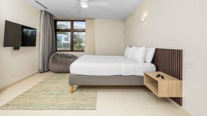Ein modernes Hotelzimmer mit Bett, Fernseher, Deckenventilator, Fenster mit Vorhängen und einem kleinen Holfnachtschränkchen.