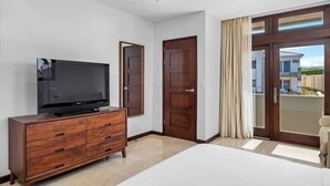 Ein modernes Hotelzimmer mit einem großen Flachbildfernseher auf einer Holzkombie, einem großen Bett und einer Schiebetür zu einem Balkon.