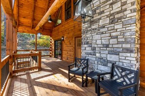 A wooden cabin with a stone wall, wooden deck, and two chairs. - New build cabin Hocking Hills | Hot tub| Sleeps 10 (Logan)