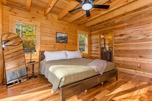 Ein Schlafzimmer einer Holzhütte mit einem Bett, einem Deckenventilator und einem großen Fenster.
