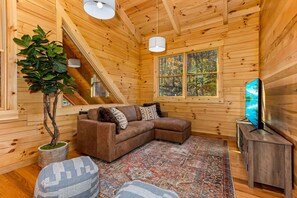 Ein gemütliches Blockhaushaus-Interieur mit Holzausstattung, einem braunen Ecksofa, einem großen Fenster und einem Fernseher auf einem Holzständer.
