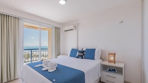 Quarto de hotel com uma cama, mesa de cabeceira, janela com cortinas e vista para o mar.
